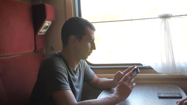 man traveler Relaxing On Train Listening To Music and smiling through the pictures via social media. slow motion video . uploading photo lifestyle using cell phone while riding home by train wagon
