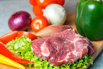 Pork-neck meat steaks on lettuce on background of radishes, tomato, red chili peppers, yellow chili peppers, green paprika, yellow paprika, red paprika, black pepper. Horizontal. Red onions, shallots