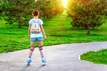 Sporting girl rollerscating in park fir alley on summer day.