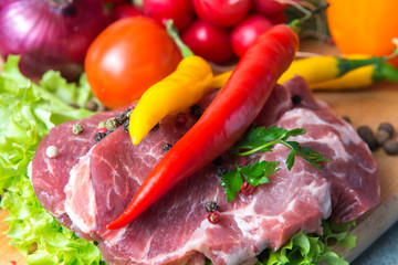 Pork-neck meat steaks on lettuce on background of radishes, tomato, red chili peppers, yellow chili peppers, green paprika, yellow paprika, red paprika, black pepper. Horizontal. Red onions, shallots