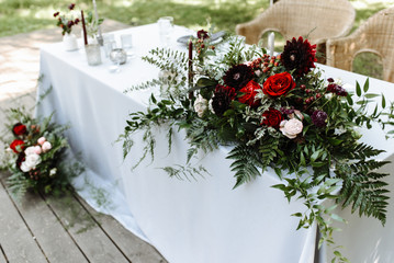 Close up of wedding table setting for newlyweds. Festive table decorated with a lot of greenery and blossom flowers and candles, outdoors