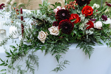 Close up of wedding table setting for newlyweds. Festive table decorated with a lot of greenery and blossom flowers and candles, outdoors