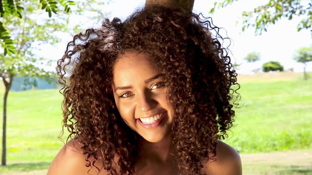 Portrait of beautiful trendy african american woman smiling at camera looking confident running hand through hair enjoying nature park. Beautiful black woman with afro hair. Brazilian girl.