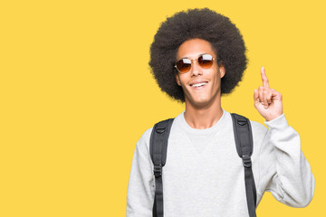 Young african american man with afro hair wearing sunglasses and backpack surprised with an idea or...
