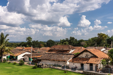 Belavadi, Karnataka, India - November 2, 2013: The red tile roof tops of the small village under blue sky with white clouds. Green vegetation band separates dwellings from sky.