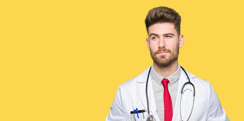 Young handsome doctor man wearing medical coat smiling looking side and staring away thinking.