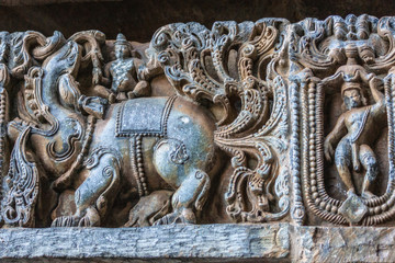 Halebidu, Karnataka, India - November 2, 2013: Hoysaleswara Temple of Shiva. Closeup of elephant and group of men statues on side of the temple structure in bluish stone and some brown background.