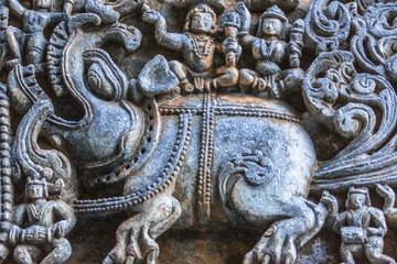 Halebidu, Karnataka, India - November 2, 2013: Hoysaleswara Temple of Shiva. Closeup of elephant and couple on top statues on side of the temple structure in bluish stone and some brown background.