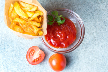 French fries, fried potatoes with ketchup and tomatoes on the background of gray-blue granite.