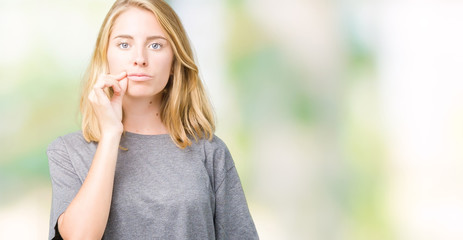 Beautiful young woman wearing oversize casual t-shirt over isolated background mouth and lips shut as zip with fingers. Secret and silent, taboo talking