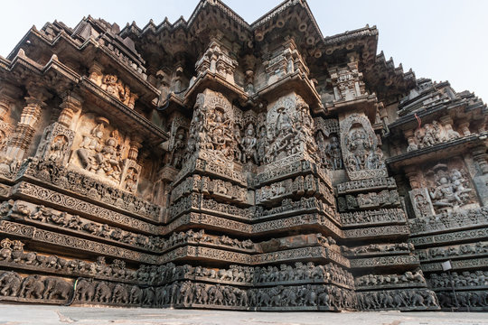 Halebidu, Karnataka, India - November 2, 2013: Hoysaleswara Temple of Shiva. Stack of ribbons of same theme statues on the Wing of temple building. Gray and brown stone against silver sky.
