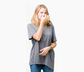 Beautiful young woman wearing oversize casual t-shirt over isolated background smelling something stinky and disgusting, intolerable smell, holding breath with fingers on nose. Bad smells concept.