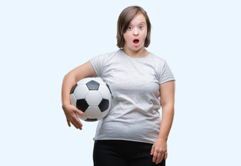 Young adult woman with down syndrome holding soccer football ball over isolated background scared in shock with a surprise face, afraid and excited with fear expression