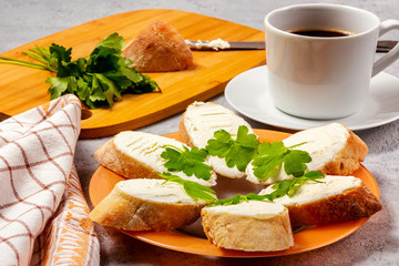 Freshly made sandwiches with cream cheese and parsley on a plate, chopping wooden board and a cup of coffee - morning and breakfast concept