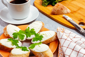 Freshly made sandwiches with cream cheese and parsley on a plate, chopping wooden board and a cup of coffee - morning and breakfast concept