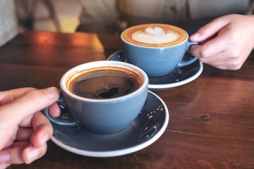 Close up image of a man and a woman clinking blue coffee mugs on wooden table in cafe