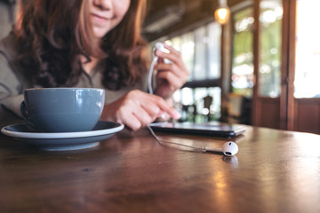 Closeup image of a woman holding earphones while listening to music with mobile phone  in cafe