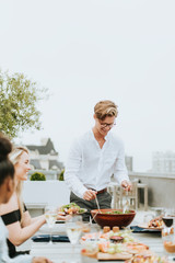 Man serving his friends salad at a rooftop party