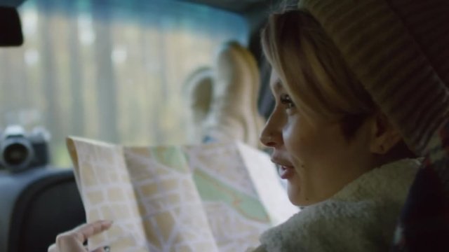 Close up face of stylish young Caucasian woman sitting in car seat and talking to driver while using map