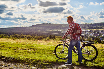 Fototapeta premium A man in nature with a bicycle on the background of mountains and blue sky