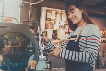 Young beautiful Asian woman barista wear blue apron holding hot coffee cup served to customer at bar counter in coffee shop with smile face.Concept of cafe and coffee shop small business.Vintage tone