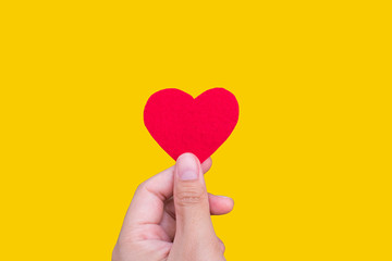 Fototapeta premium Small heart in hand against yellow background, Giving love for Valentine’s Day