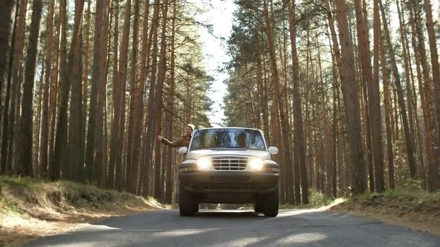 Front view of silver crossover car approaching camera, young woman looking out of window and enjoying fresh air and views of forest