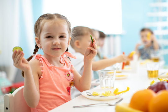 Adorable kid girl eating vegetables in kindergarten