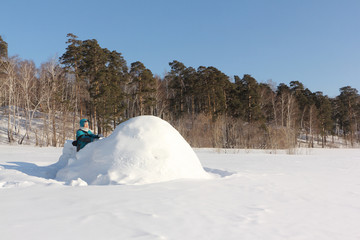 Happy woman a red jacket building an igloo on a snow glade in the winter,  Siberia, Russia