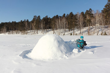 Happy woman in warm clothes building an igloo on a snow glade in the winter,  Siberia, Russia