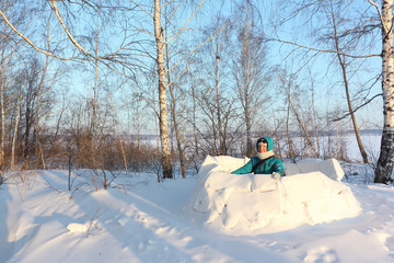 Happy woman in warm clothes sitting in an unfinished  igloo on a snow glade in the winter,  Siberia, Russia