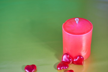 Red wax festive romantic candle on a green decorative background and red glass zerdechki near. love symbol. festive mood. romantic dinner. copy space
