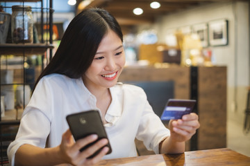 Young beautiful asian woman using smart phone and credit card for shopping online in coffee shop cafe