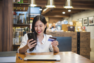 Young beautiful asian woman using smart phone and credit card for shopping online in coffee shop cafe