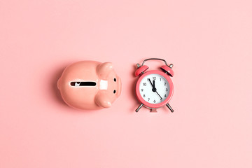 Piggy bank and classic alarm clock on pink background. Time to saving, money, banking concept.  Flat design, top down composition. - obrazy, fototapety, plakaty