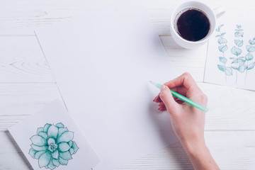  Flat lay with women hand writing on blank paper with coffee cup and green painted cards on a white wooden background. Instagram and business concept. Copy space