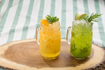 Set cold lemonade with lemon, orange and kiwi on wooden board on striped textile background