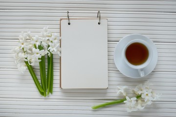 Spring tea. Spring Flat lay.Spring to-do list.White hyacinth flower, cup of tea  and blank notebook on a white wooden grooved board background. top view, copy space.