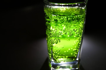 bright lucent green fizzy drink (lemonade, cocktail) with many small bubbles in dark closeup