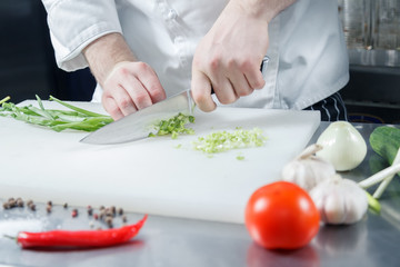 Obraz na płótnie Canvas Closeup chef's hands cooking green onion for preparing healthy vegetable salad on acutting board in restaurant kitchen. Concept new lean menu, low calories speciality