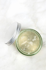 A photo of a glass jar with aloe vera gel, shot from above on a white marble background with copy space