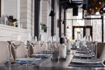 Restaurant interior, serving, wine and water glasses, plates, forks and knives on textile napkins stand in a row on vintage gray wooden table. Concept banquet, birthday, conference, group lunch