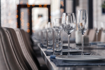 Restaurant interior, serving, wine and water glasses, plates, forks and knives on textile napkins stand in a row on vintage gray wooden table. Concept banquet, birthday, conference, group lunch