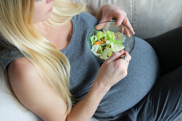 Healthy, Young, Pregnant Woman Sitting on Couch Eating Green Lettuce Salad