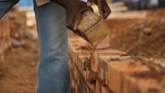 Black construction worker places bricks in wall with cement