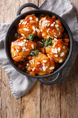 Fried glazed chicken thighs with dried apricots and almonds closeup in a pan. Vertical top view