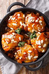 Tender sticky chicken thighs with apricot glaze and almond flakes close-up in a pan. Vertical top view