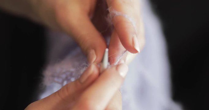 Top-down macro close-up view of female hands slowly knitting against a black background