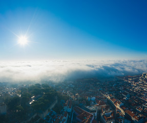 Fototapeta na wymiar Aerial; panoramic drone view of foggy Lisbon morning; impending clouds over the ancient ginger roofs; blue skyline and bright sun in portuguese historical capital; touristic areas, old narrow streets
