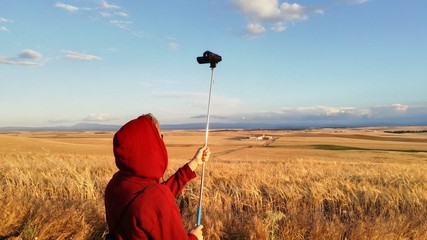Young boy recording a video of agrarian landscape. Fields sown with wheat and barley growing as far as the eye can see on the horizon. Natural blue sky totally calm in a summer afternoon.